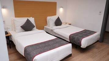 Habitación de hotel con dos camas individuales, cabecero de madera, mesitas de noche y una mesita auxiliar.