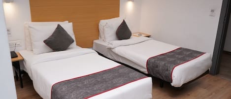 A hotel room with two single beds, wooden headboard, bedside tables, and a nightstand.