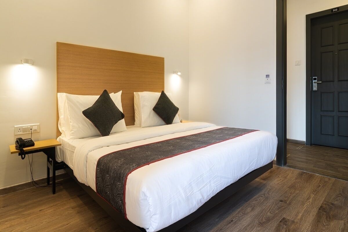 Una habitación de hotel con cama, mesita de noche y puerta.