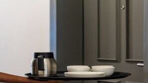 Un plateau noir sur lequel se trouvent une cafetière et des bols blancs, que tient une personne.