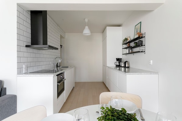 Une cuisine moderne avec des meubles blancs, une hotte noire et un luminaire suspendu blanc.