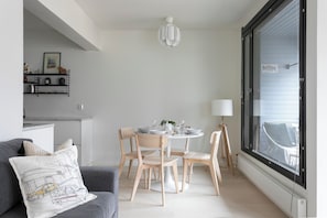 Un salon moderne avec un canapĂ© gris, des chaises en bois, une table de salle Ă manger ronde et une grande fenĂȘtre avec des stores.