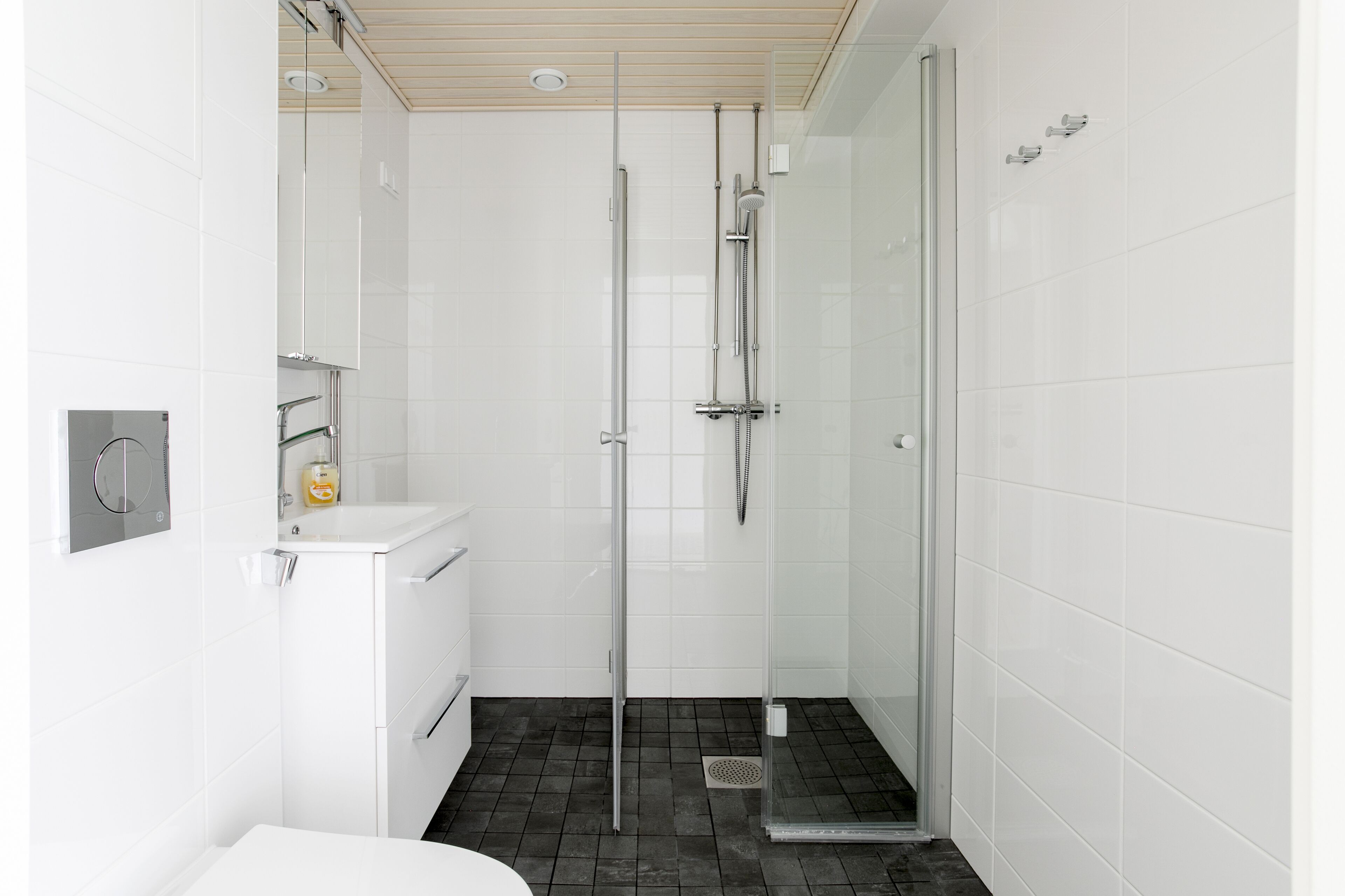 Een moderne badkamer met een douche met glazen wand, witte tegels en een wit wastafel.
