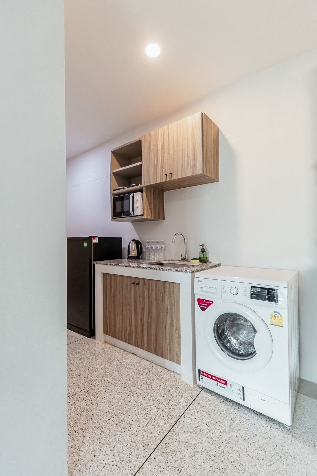A compact kitchen with wooden cabinets, a built-in microwave, a washing machine, and a small countertop.
