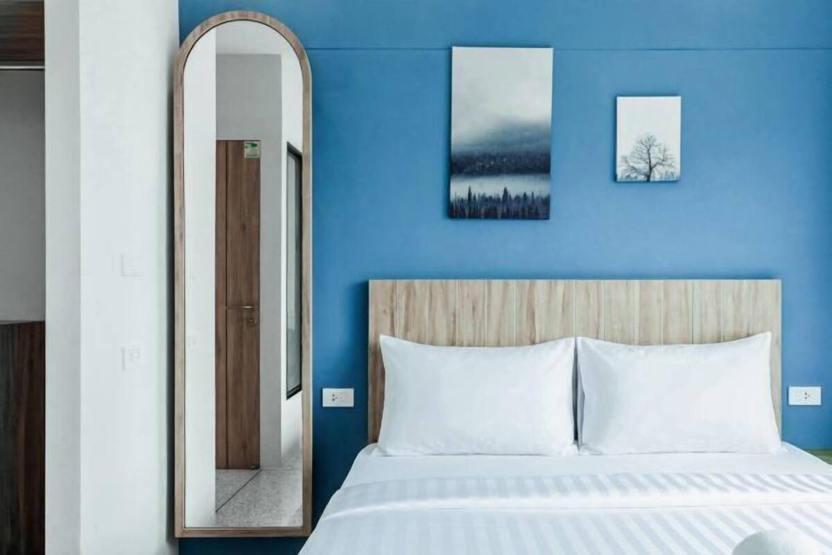A bedroom with a bed, a wooden headboard, a large mirror, and two wall art pieces.