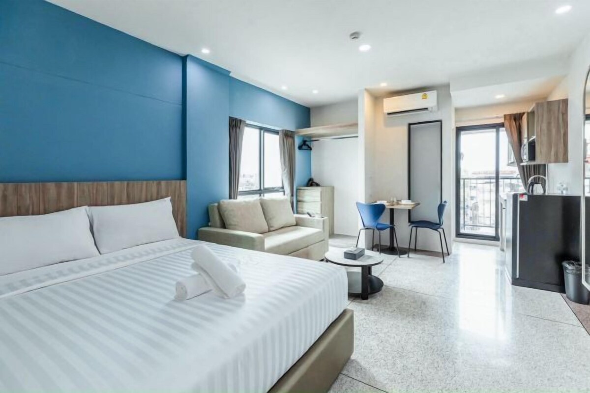 A modern hotel room with a bed, a seating area with a table and chairs, and a kitchenette.