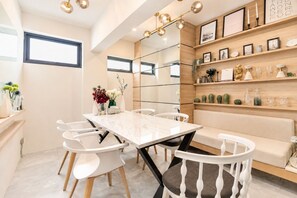 A modern dining area with a marble table, white chairs, a wooden bench, and a wall-mounted shelf with decorative items. - ABC@48 Hotel & Service Apartment (Bangkok)