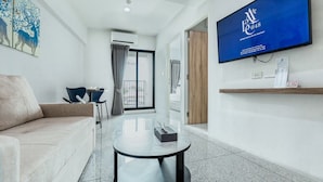 A modern hotel room with a sofa, a round table, a TV, and a view of the outside. - ABC@48 Hotel & Service Apartment (Bangkok)