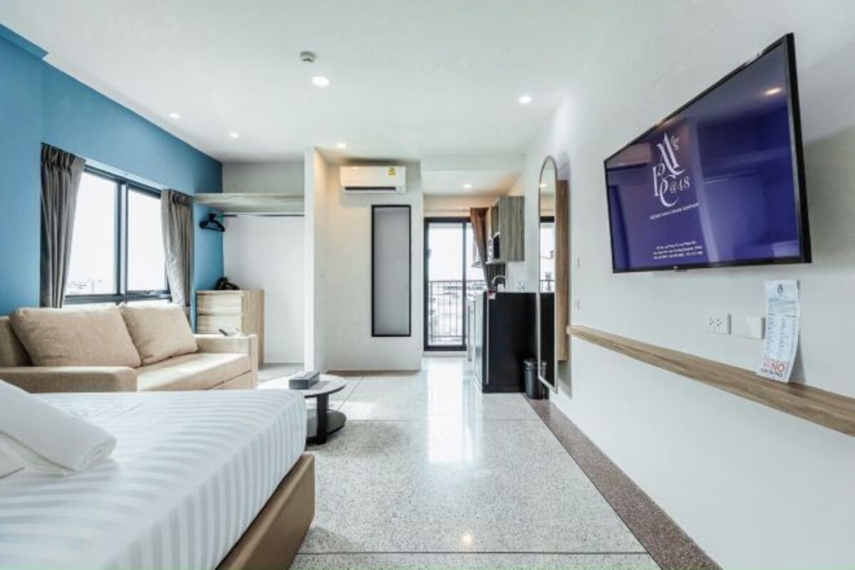 A hotel room with a bed, a sofa, a TV, and a kitchenette.
