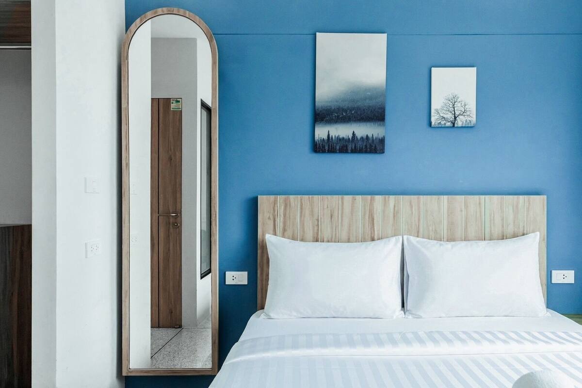 A hotel room with a large mirror, a bed with white bedding, and two wall-mounted paintings.