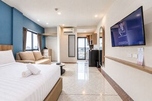 A hotel room with a bed, a sofa, a TV, and a view of the city. - ABC@48 Hotel & Service Apartment (Bangkok)