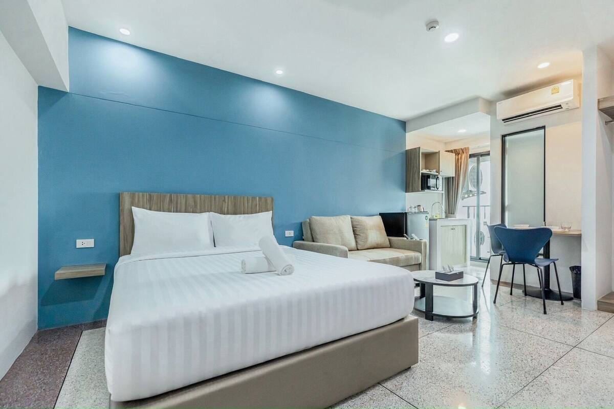 A modern hotel room with a large bed, a sofa, a desk, and a mirror.