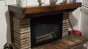 A fireplace with a stone surround, a shelf above with decorative items, and a potted plant on the floor. - Quiet apartment in the coutryside of Marche (Cagli)