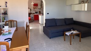 A modern living room with a dining area, a grey sofa, a wooden dining table, and a kitchen in the background. - Quiet apartment in the coutryside of Marche (Cagli)