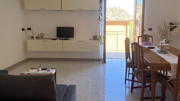 A living room with a sofa, a TV on a low wall, a dining table with chairs, and a view of the outside. - Quiet apartment in the coutryside of Marche (Cagli)