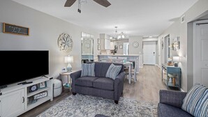 Un salon moderne avec un téléviseur à écran plat, un canapé gris, un tapis à motifs et un ventilateur de plafond.