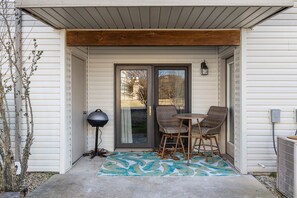 A covered patio with a table and chairs, a grill, and a decorative rug. - No-Step 2BR | 2 Kings | Indoor Pool + Hot Tub (Branson)