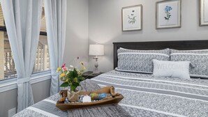 Une chambre à coucher bien rangée, avec un lit, une table de chevet dotée d’une lampe et un plateau contenant des objets décoratifs.