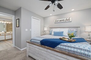 A bedroom with a bed, a ceiling fan, a bedside table, a nightstand, a mirror, a door, and a wall with a motivational quote. - No-Step 2BR | 2 Kings | Indoor Pool + Hot Tub (Branson)