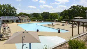 Une piscine entourée de verdure, agrémentée de chaises longues et de parasols, et à proximité d’un bâtiment équipé de panneaux solaires.