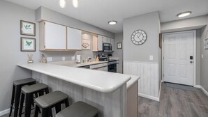 Une cuisine moderne avec un coin bar, des meubles en bois, un four à micro-ondes et une horloge murale.