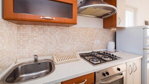 Eine Küche mit Spüle aus Edelstahl, einem Gasherd, Holzschränken und einer gefliesten Spritzschutzwand.