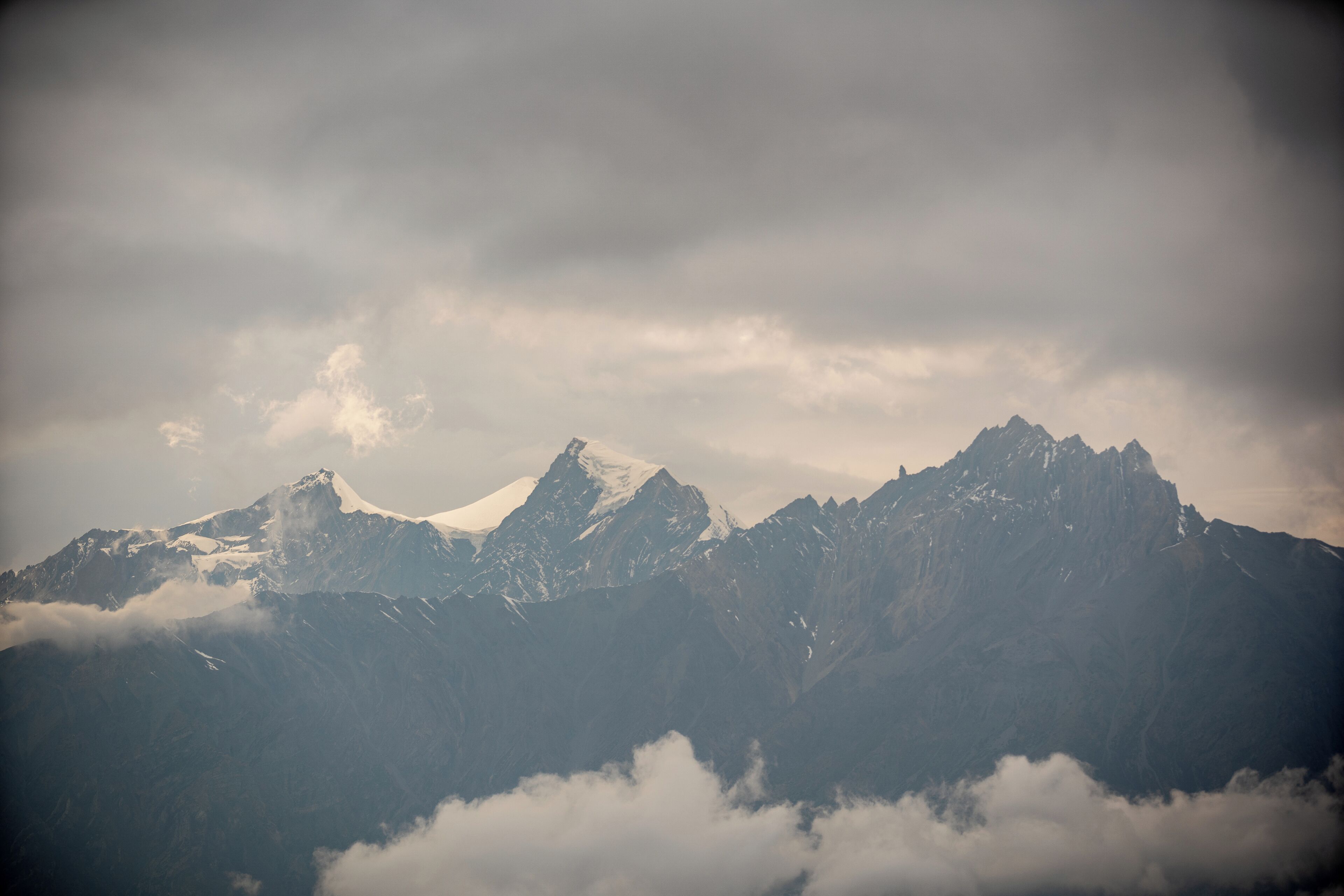 A mountain range with snow-capped peaks and clouds below.
