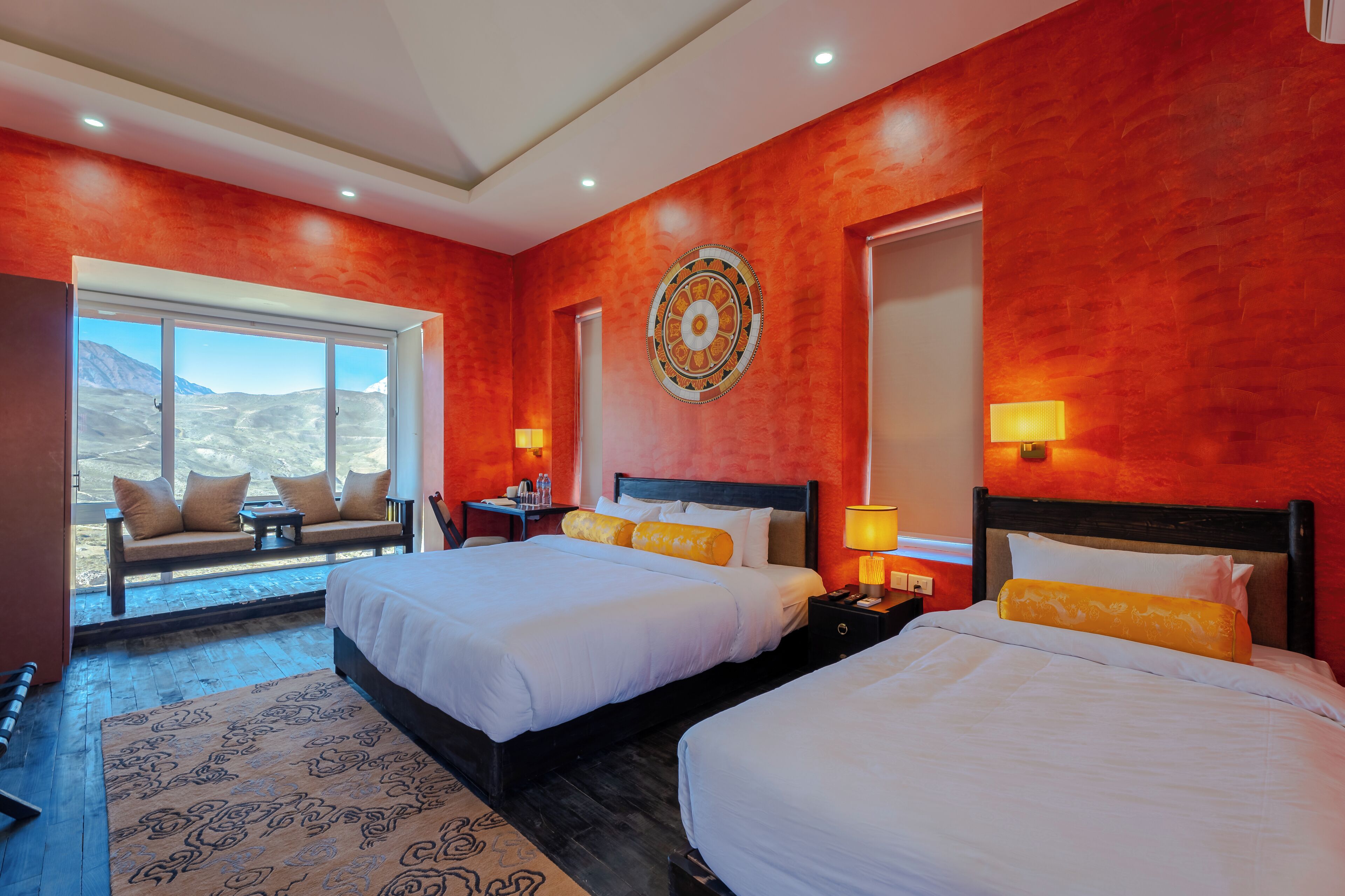A hotel room with two beds, a sofa, a large window with a view, and a decorative wall piece.
