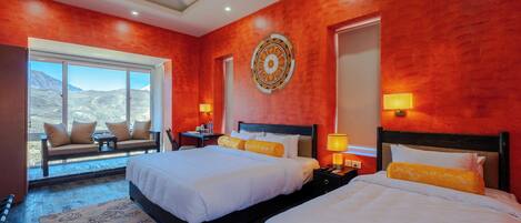 A hotel room with two beds, a sofa, a large window with a view, and a decorative wall piece.