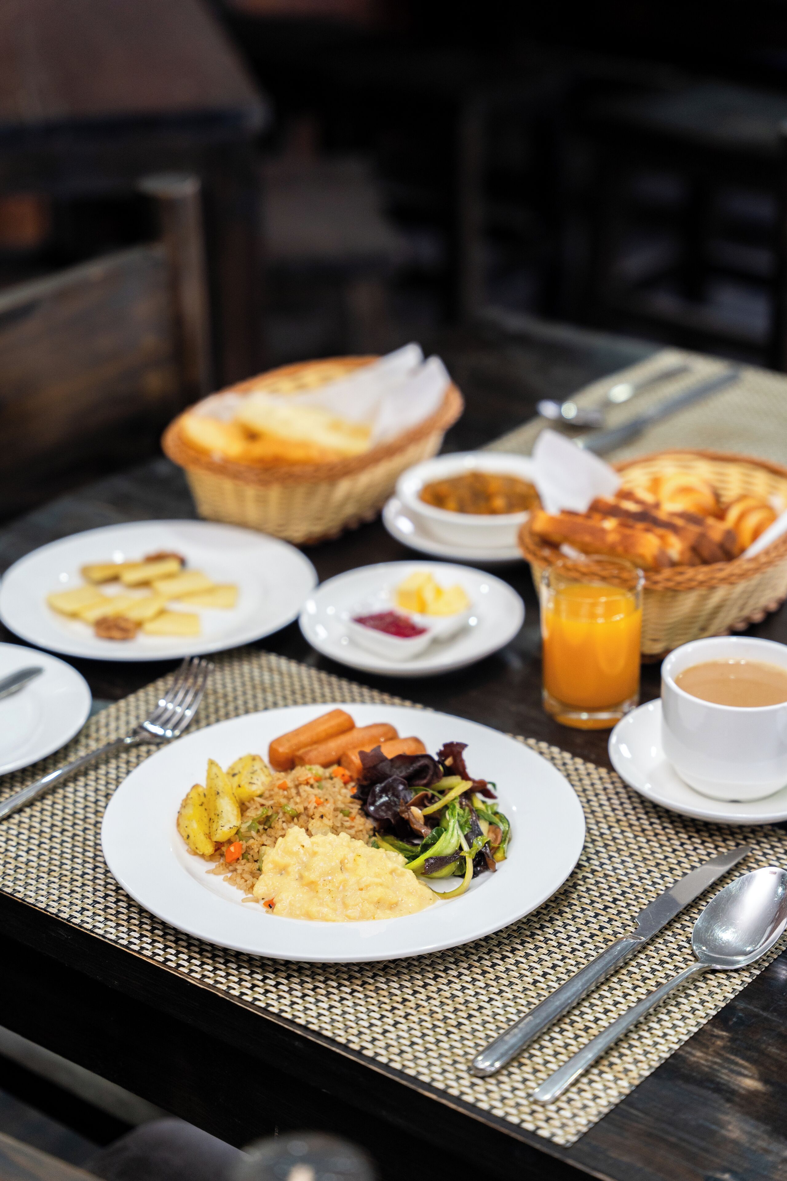 Et morgenbord med tallerkener mad, en kurv med brød, et glas appelsinjuice og en kop kaffe.