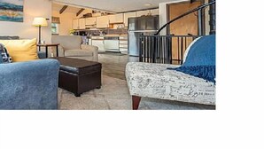 A living room with a sofa, ottoman, and a patterned armchair. A staircase is visible in the background leading to an upper floor. - In the Heart of Deep Creek, Wood Fire, steps Lake, Coffee, Pizza, minutes Whisp, (Oakland)