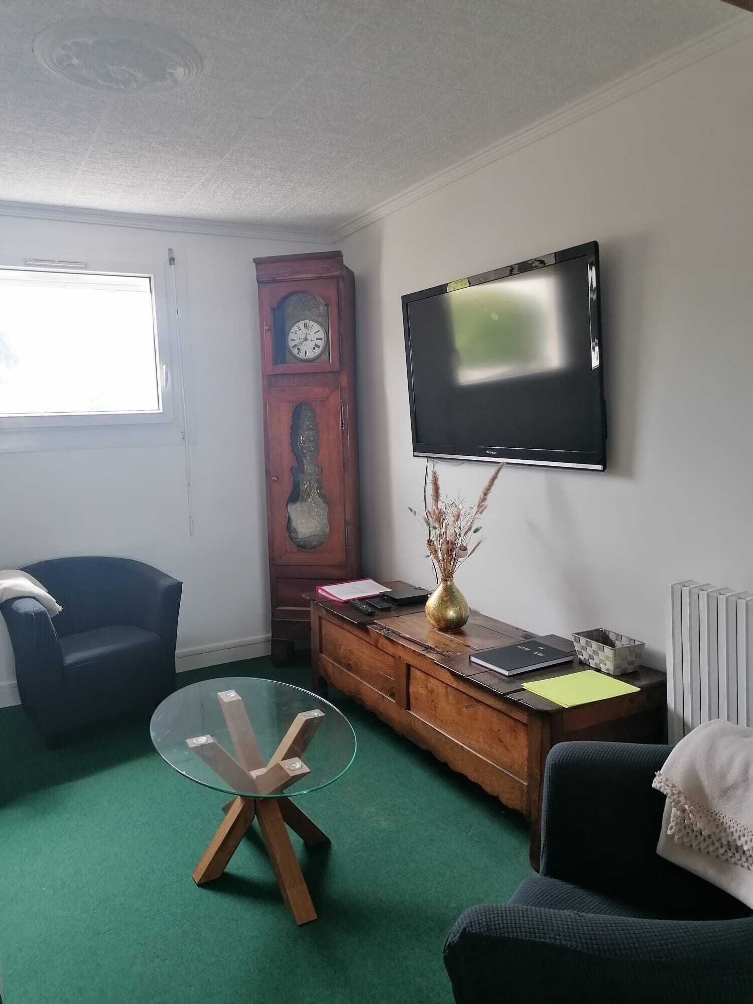 Ein Zimmer mit einem Holzkoffer, einem an der Wand befestigten Fernseher, einem Glastisch und zwei Stühlen.
