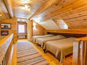Un dormitorio acogedor en el ático con paredes de madera y techo inclinado, que cuenta con dos camas y una ventana.
