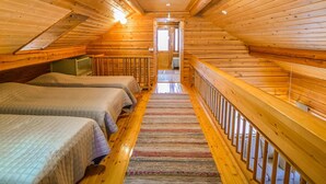 A cozy attic bedroom with two beds, a wooden ceiling, and a view of the outside.
