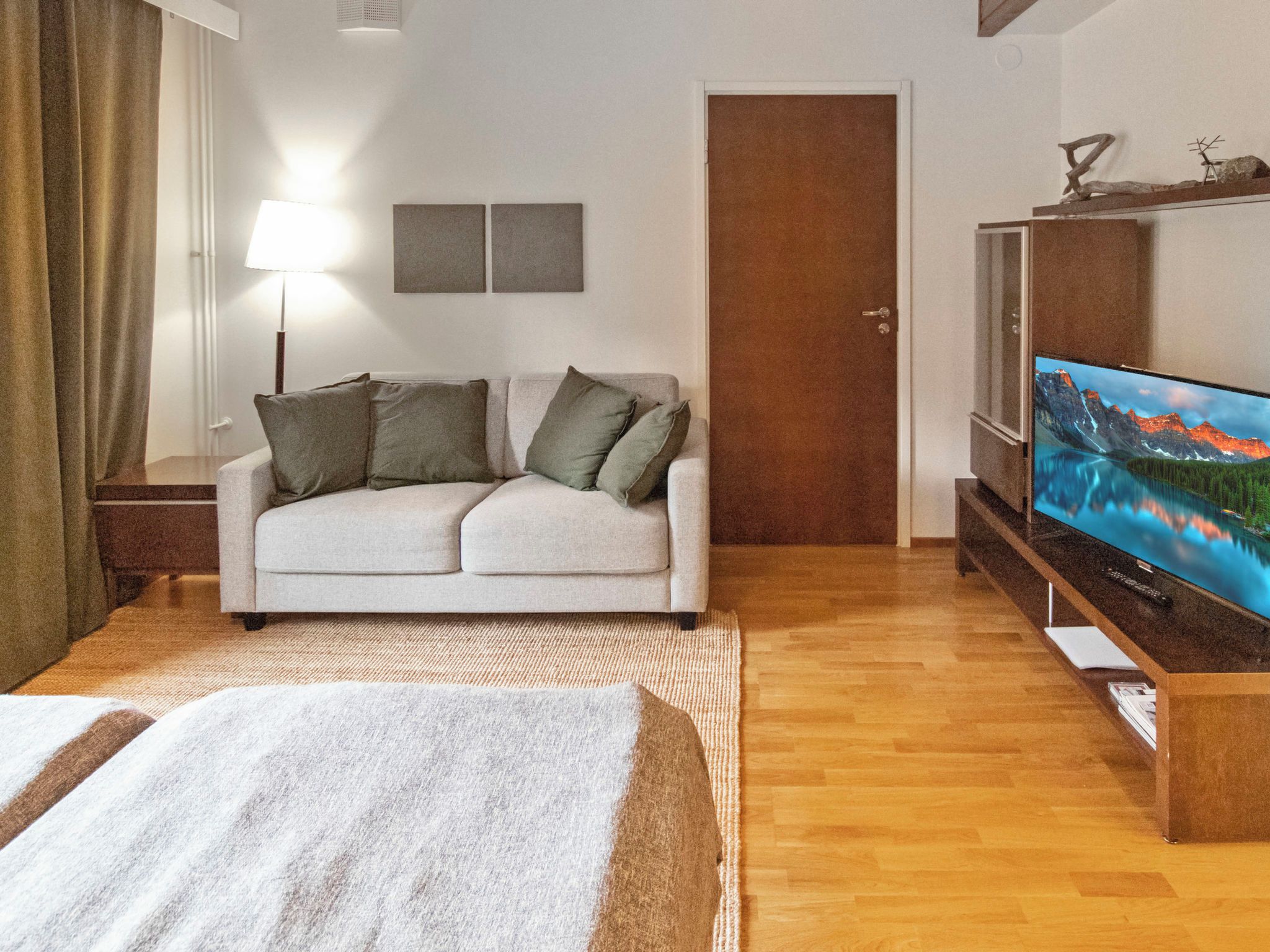 Un soggiorno con un divano, una TV, una lampada e una porta.