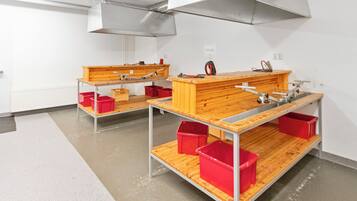 A workshop with two workbenches, red storage bins, and overhead ventilation.