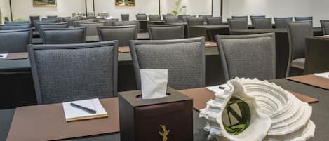 A hotel conference room with rows of gray chairs, a tissue box, and a decorative shell on the table.