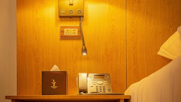 A wooden bedside table with a lamp, a tissue box, and a telephone.