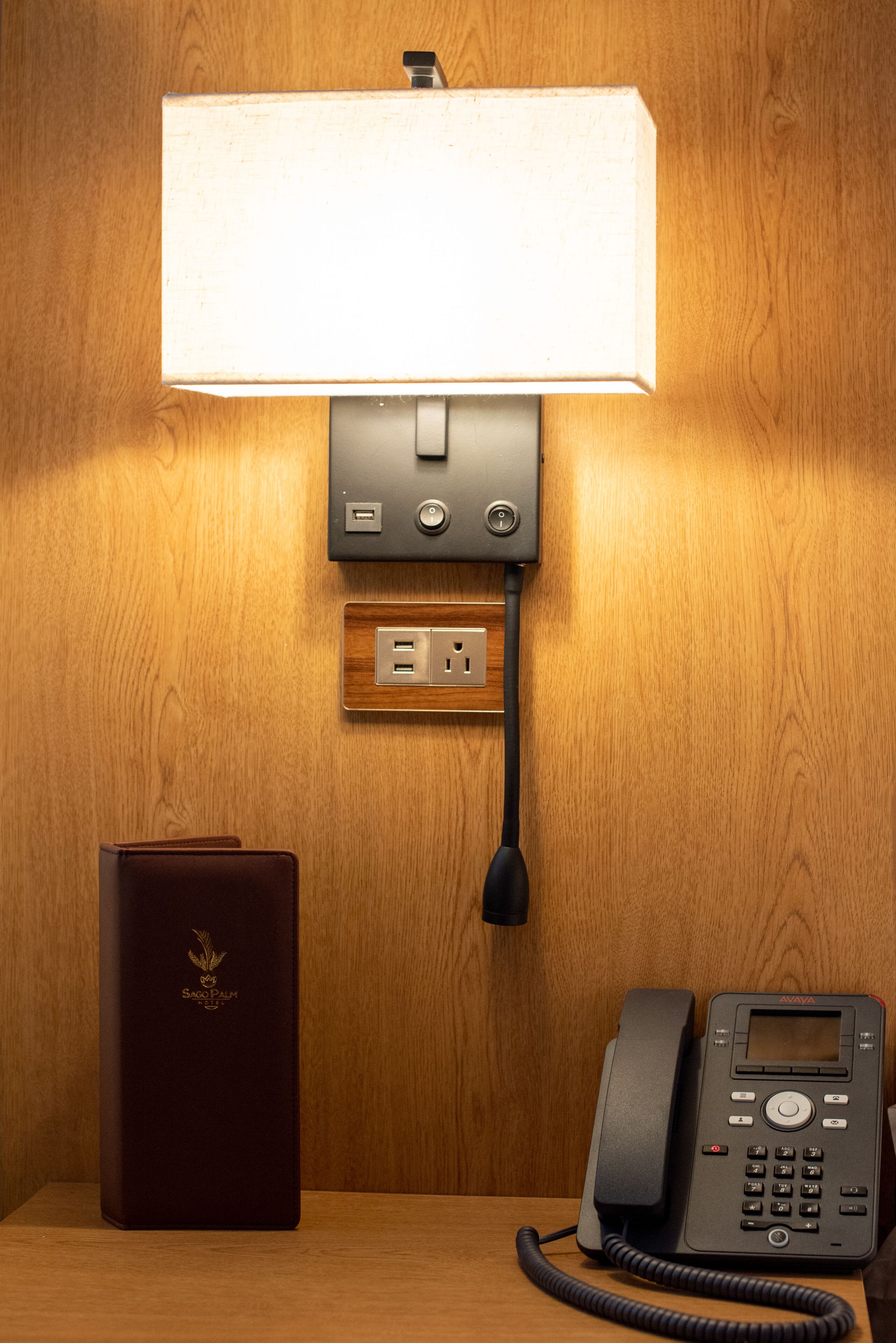 Een houten wand met een wandlamp, een telefoon en een stopcontact.
