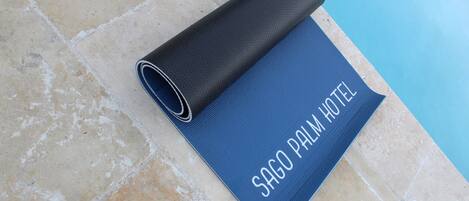 A blue mat with "SAGO PALM HOTEL" text on a tiled floor near a pool.