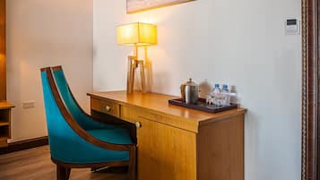 Ein Hotelzimmer mit Holztisch, einem stuhlförmigen Sessel in Türkis, einem Bild an der Wand, einer Lampe und einem Wasserspender.