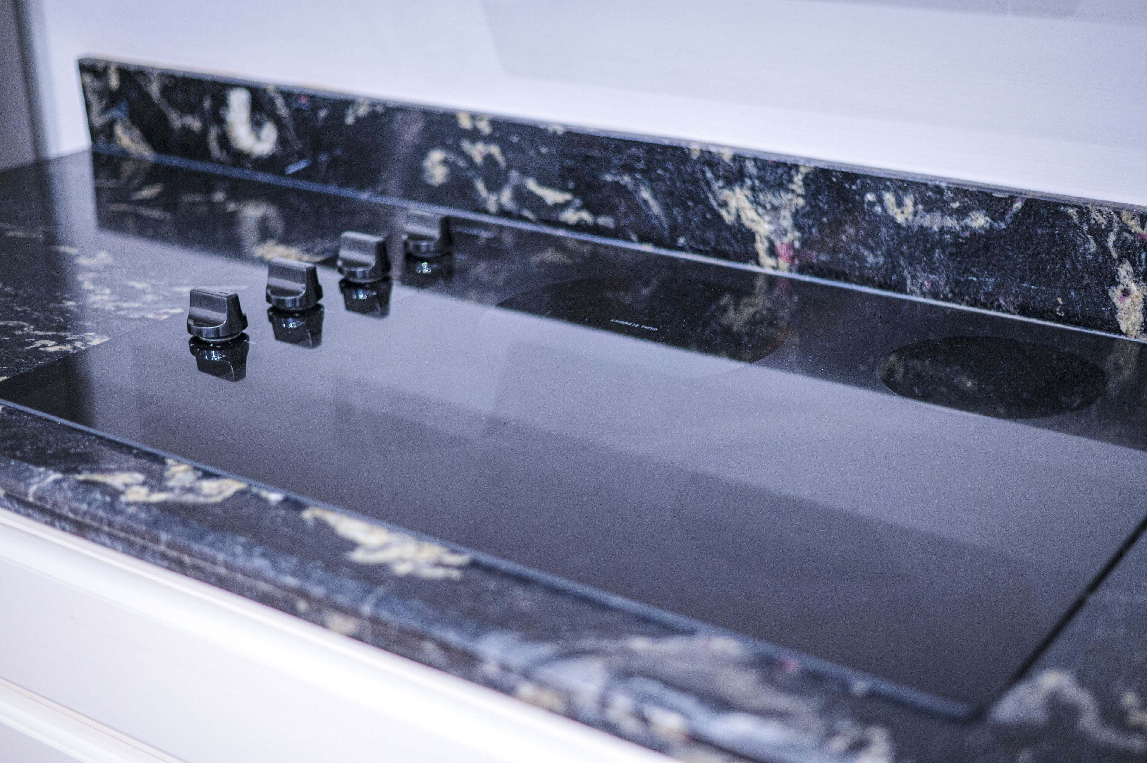 A kitchen with a black marble countertop and four black knobs.