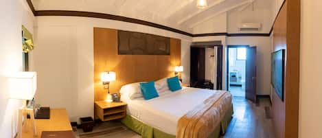 Una camera d'albergo con un letto grande, lampade sui comodini, una testiera in legno, una scrivania con lampada, un tavolino e una porta che dà su un bagno.