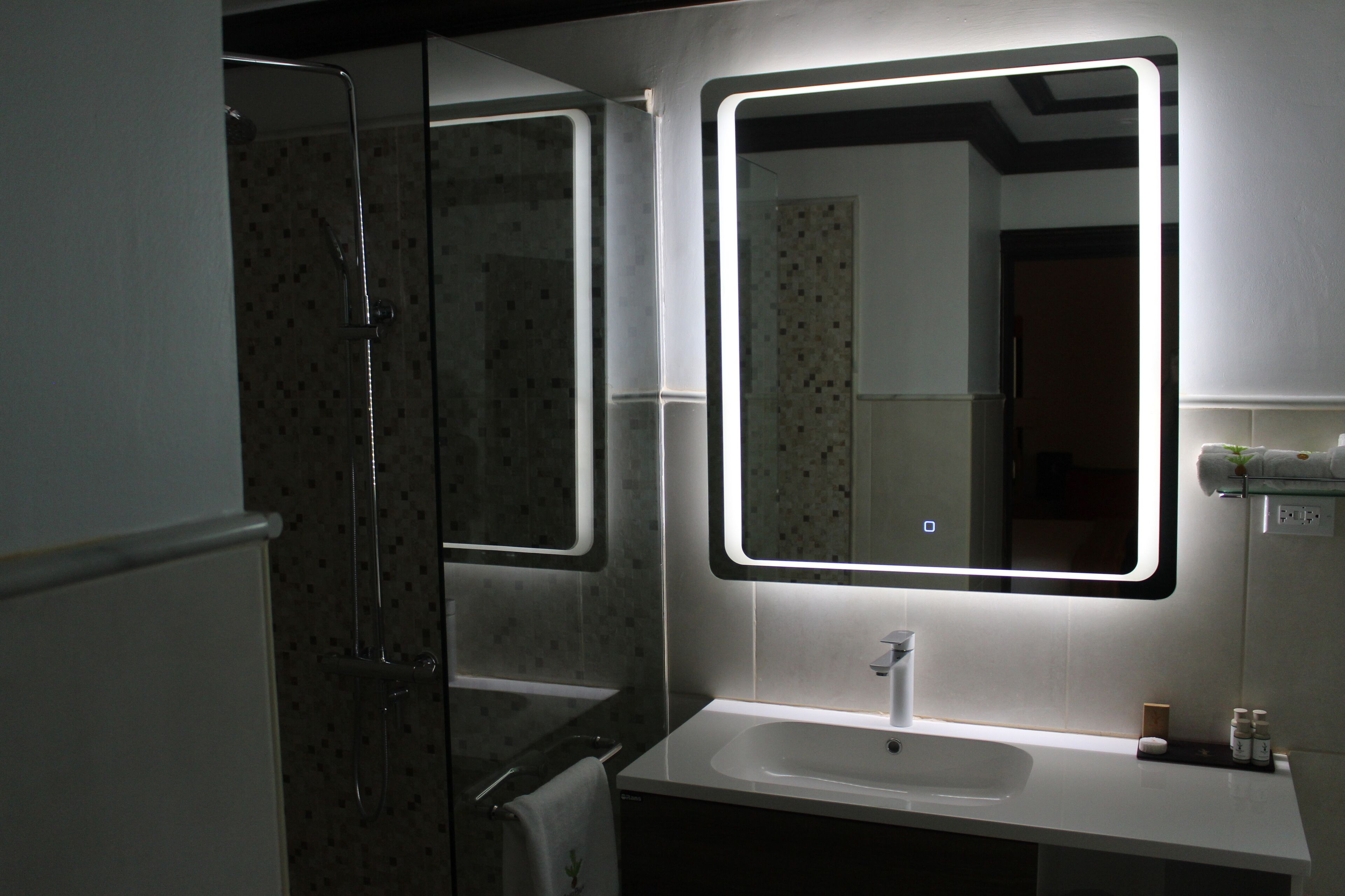 A modern bathroom with a glass shower enclosure, a white sink, and a mirror with LED lighting.