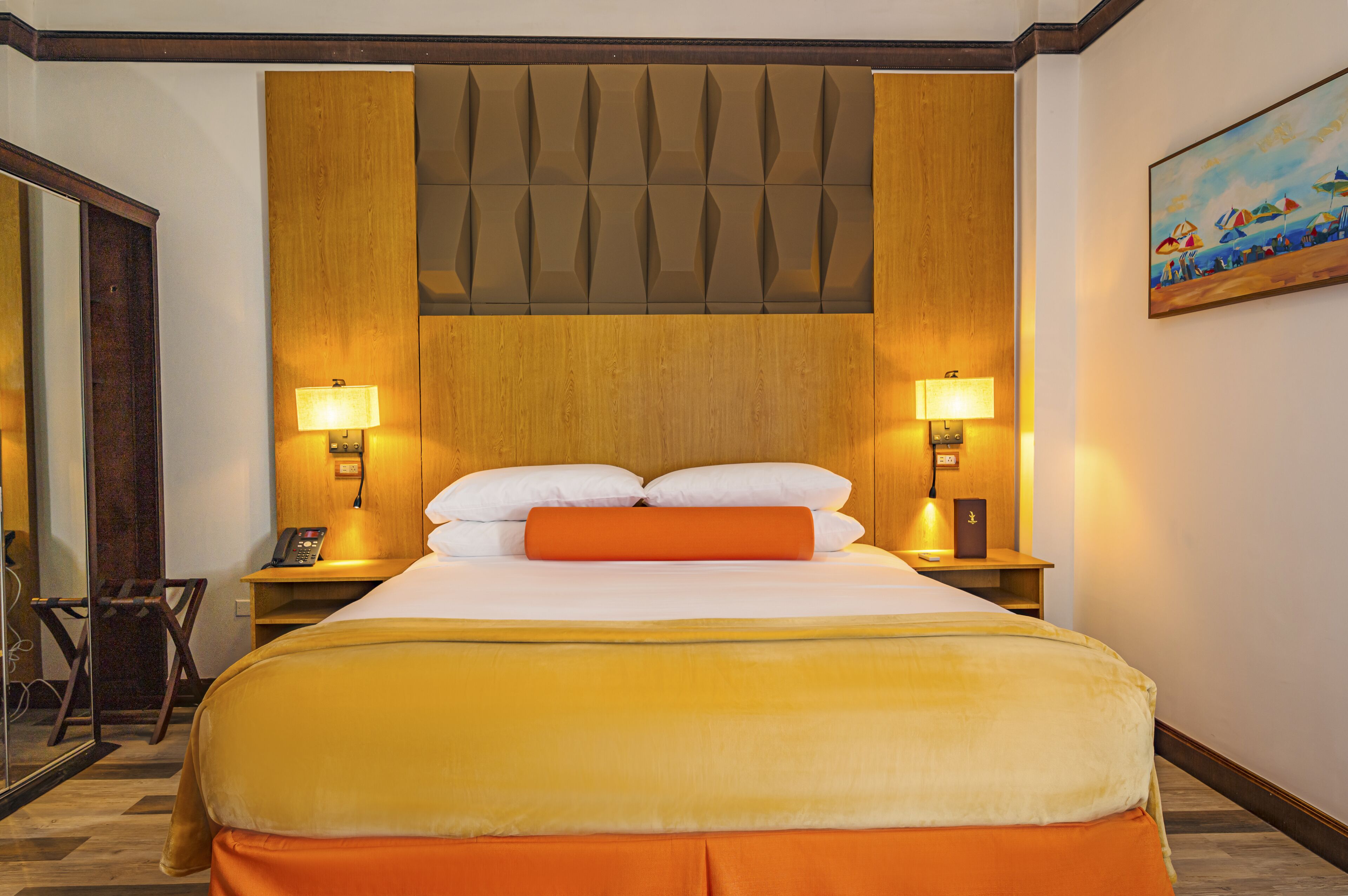 Ein Hotelzimmer mit einem großen Bett, zwei Nachttischlampen, einem Holzkopfstück und einem Gemälde an der Wand.