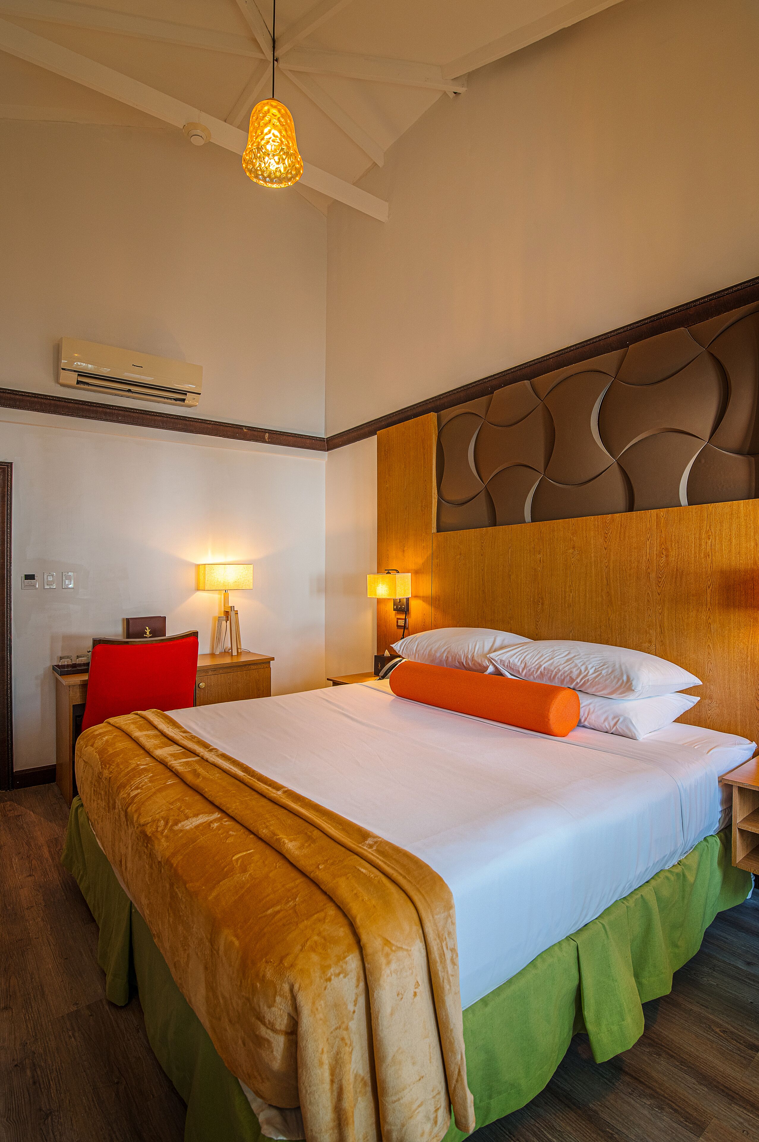 A hotel room with a large bed, a desk, a chair, and a lamp.
