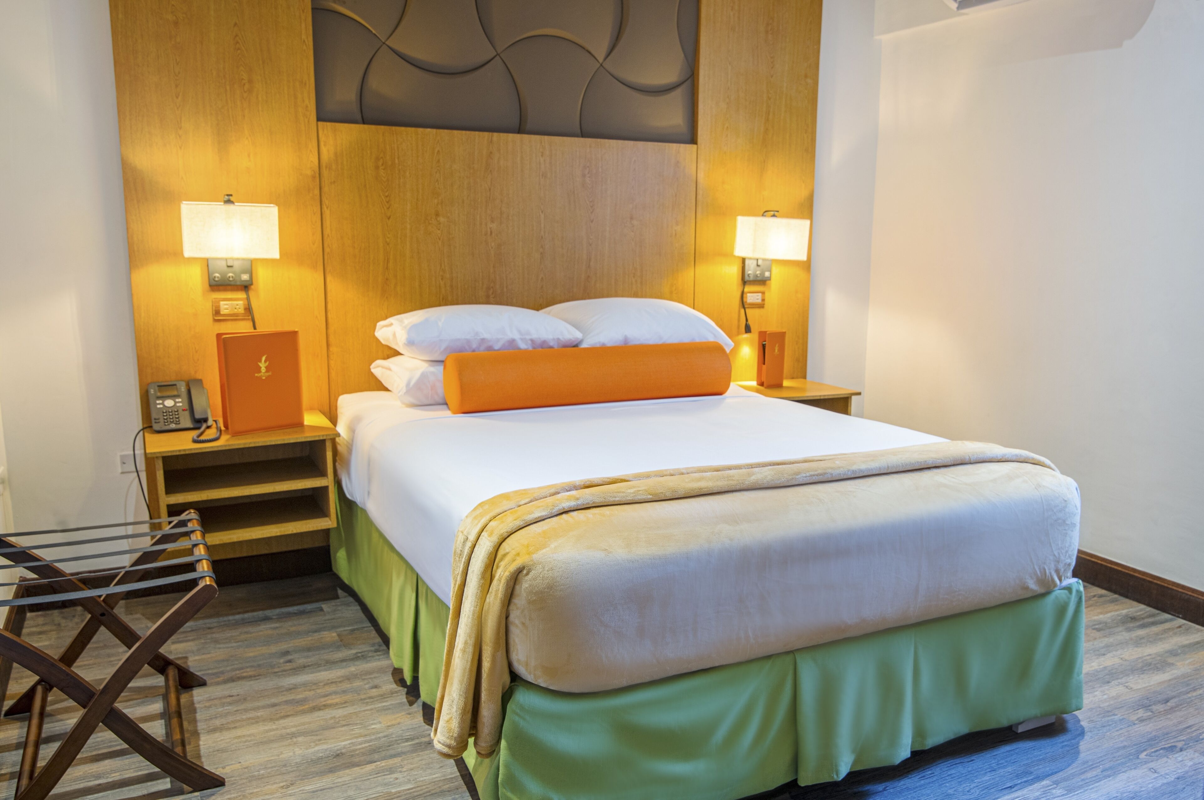 A hotel room with a large bed, two bedside tables with lamps, a telephone, and a drying rack.