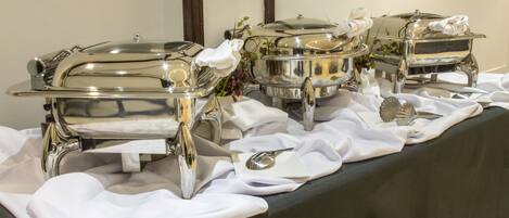 Montaje de bufé con múltiples fuentes de plata sobre una mesa cubierta con mantel negro y manteles blancos.