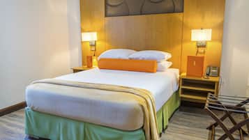 A neatly made bed with a green skirt, two bedside lamps, a telephone, and a wooden nightstand.