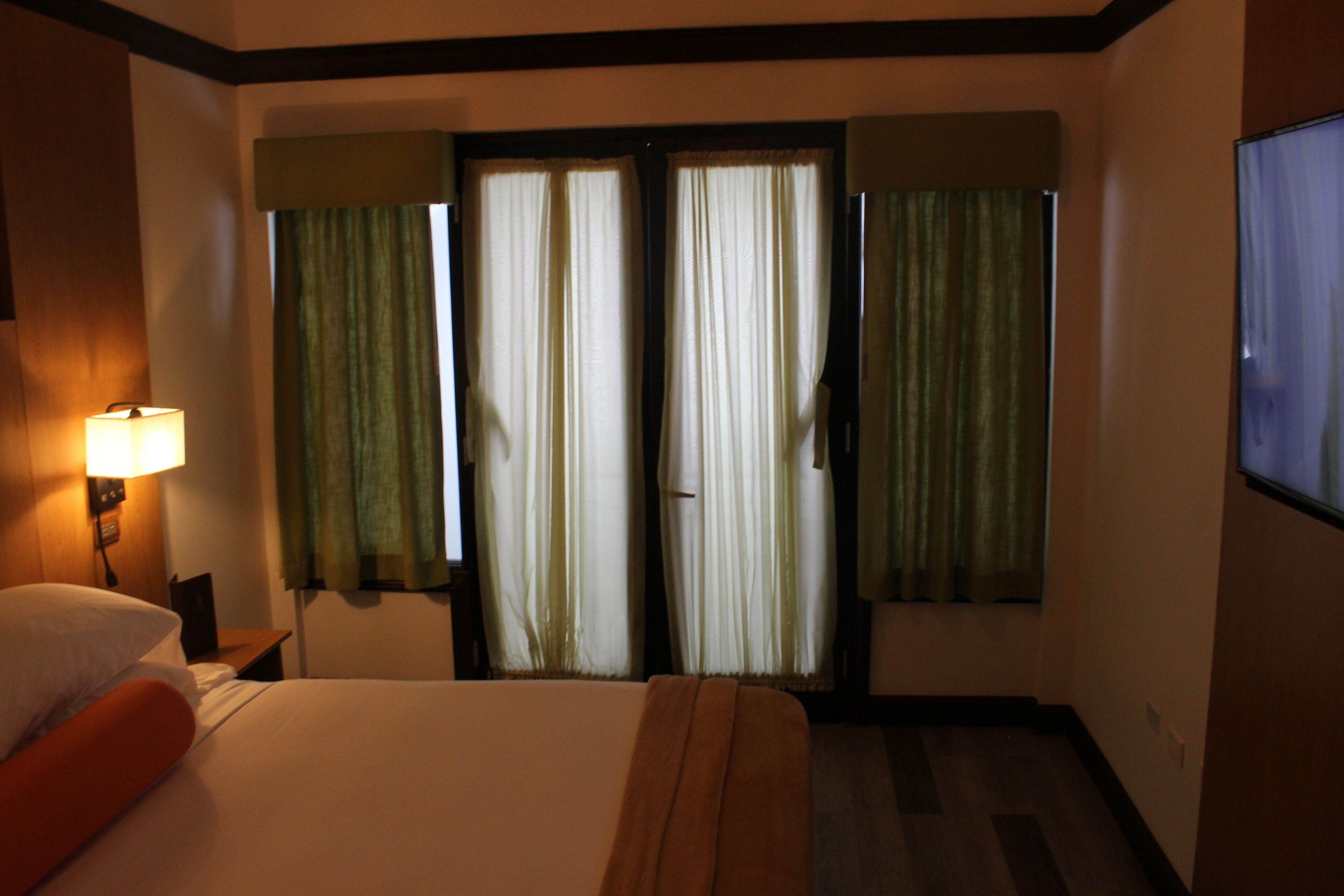 Una habitación de hotel con cama, una mesita de noche con lámpara y un televisor en la pared.